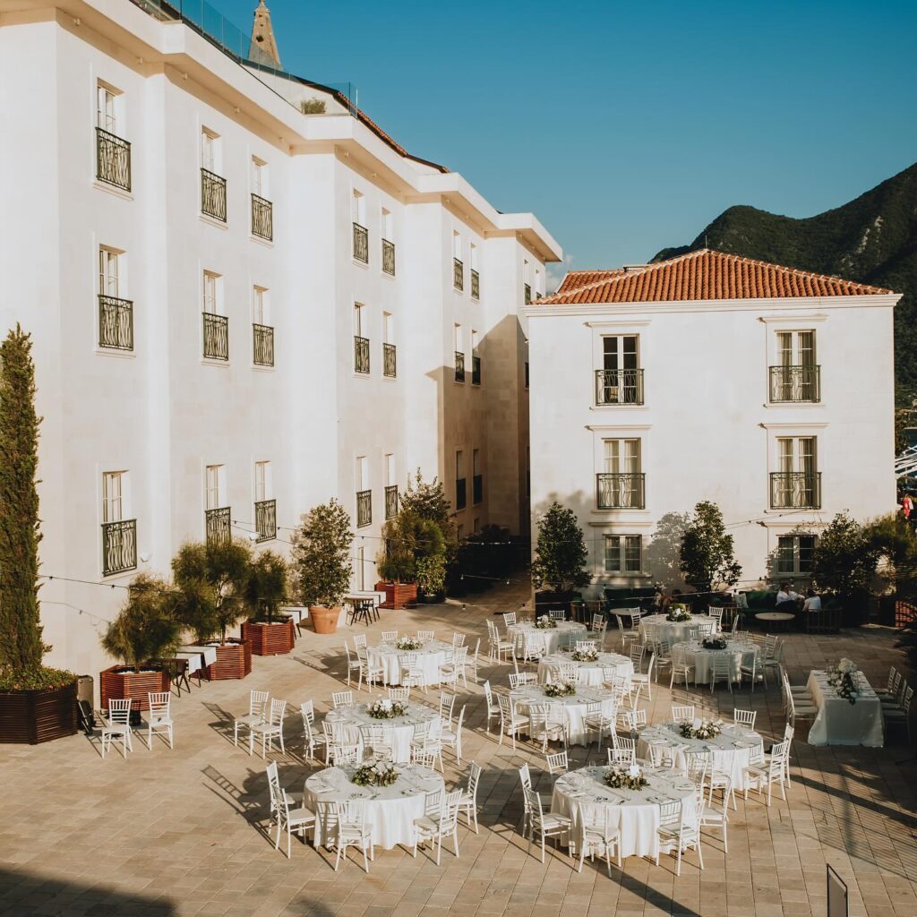 Courtyard wedding reception setup with round tables at Grand Heritage Perast, with mountains in the background.