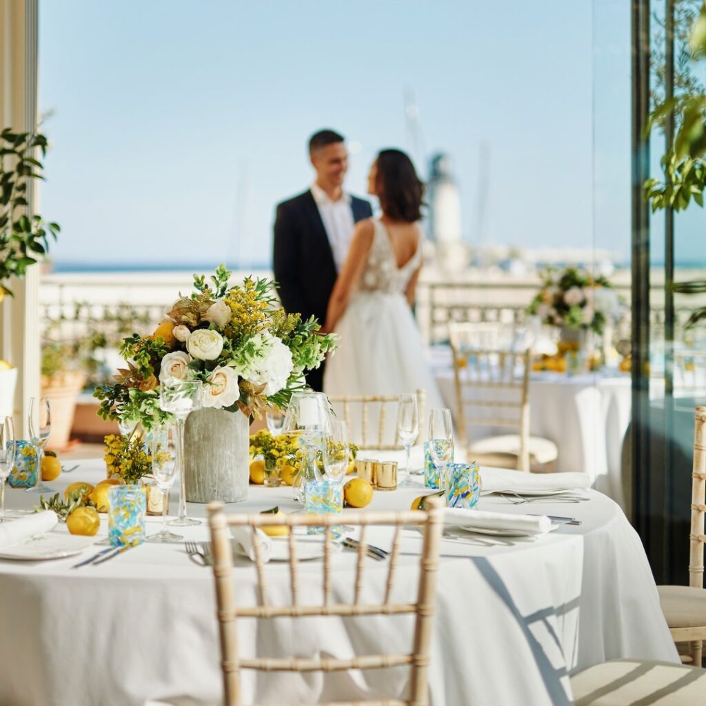 Wedding table styling on a sea-view terrace at The Chedi Luštica Bay, Montenegro, with the couple in the background.
