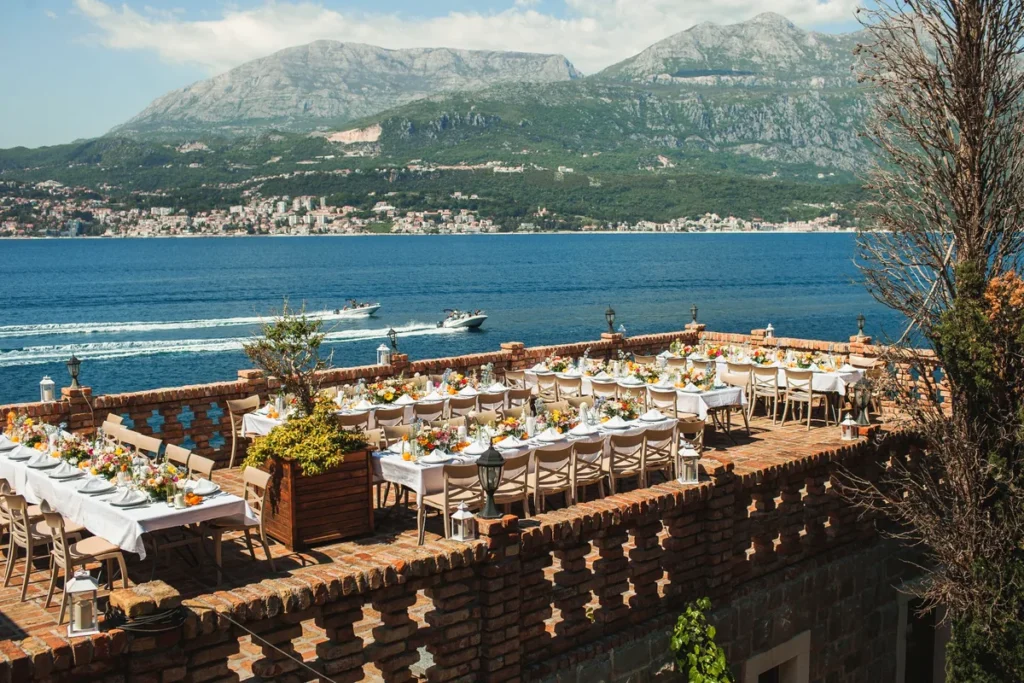 Evening wedding dinner with guests and candlelight on the waterfront terrace at Forte Rose, Rose village, Montenegro.