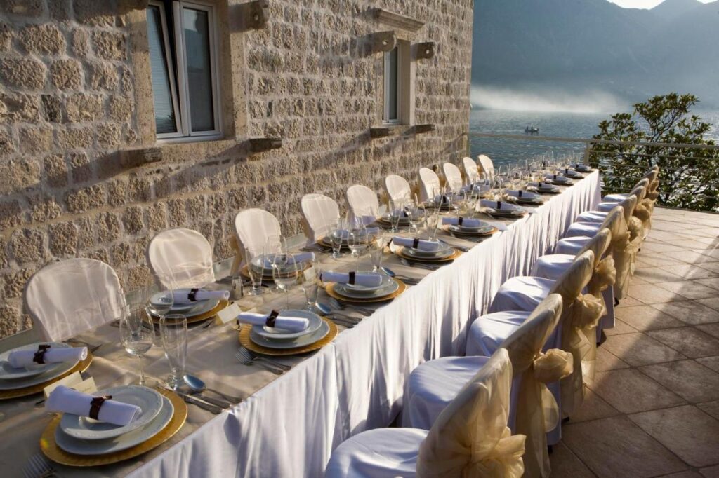 Long wedding dinner table on the roof terrace beside a stone wall with views of Kotor Bay at Palazzo Radomiri, Montenegro.