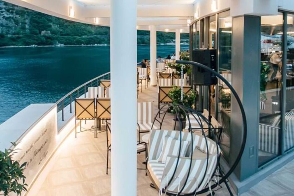 Bay-view terrace at Verige65 Restaurant & Bar in Kostanjica with cruise ship in the background, Boka Bay, Montenegro.