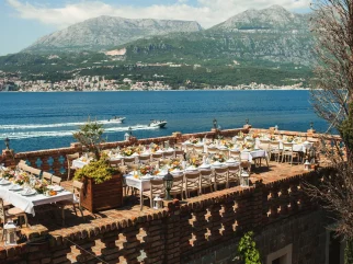 Evening wedding dinner with guests and candlelight on the waterfront terrace at Forte Rose, Rose village, Montenegro.