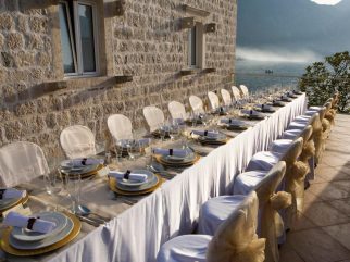 Long wedding dinner table on the roof terrace beside a stone wall with views of Kotor Bay at Palazzo Radomiri, Montenegro.